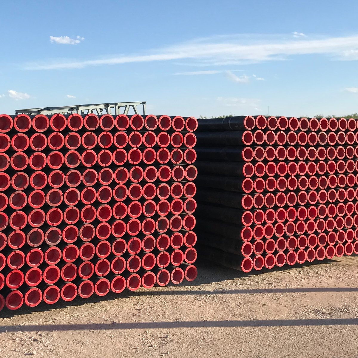 Stacks of finished TSC drill pipe with thread protectors on location.